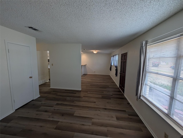 hall with dark hardwood / wood-style floors, a textured ceiling, and a wealth of natural light