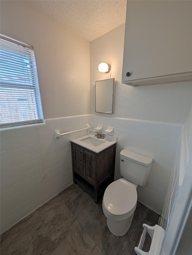 bathroom with vanity, toilet, a textured ceiling, and tile walls