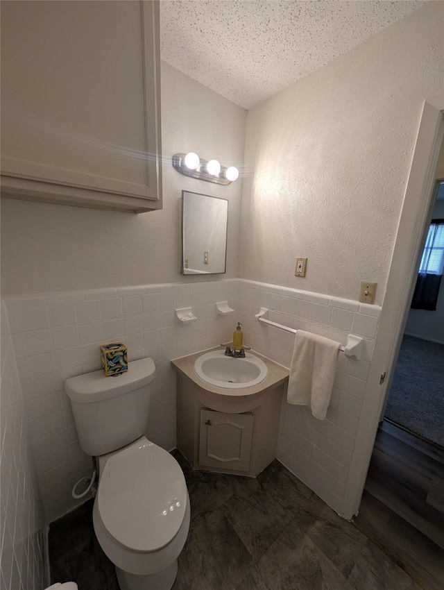 bathroom featuring a textured ceiling, vanity, toilet, and tile walls