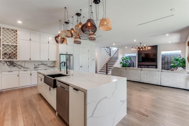 kitchen with pendant lighting, a center island with sink, sink, appliances with stainless steel finishes, and white cabinetry