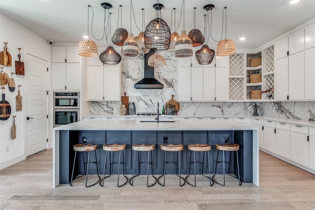 kitchen featuring a center island with sink, wall chimney range hood, and hanging light fixtures