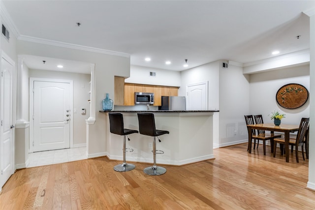 kitchen featuring a kitchen bar, light hardwood / wood-style flooring, ornamental molding, appliances with stainless steel finishes, and kitchen peninsula