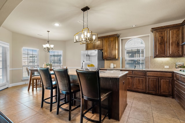 kitchen with high end refrigerator, tasteful backsplash, light stone counters, a chandelier, and a center island