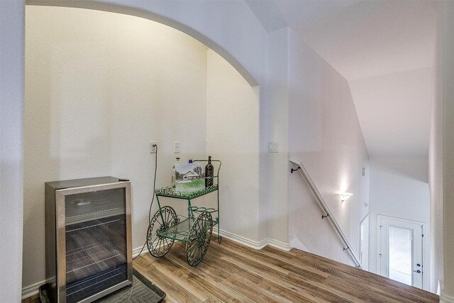 staircase featuring hardwood / wood-style floors, vaulted ceiling, and beverage cooler