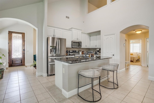 kitchen featuring a center island with sink, dark stone countertops, light tile patterned floors, white cabinetry, and stainless steel appliances