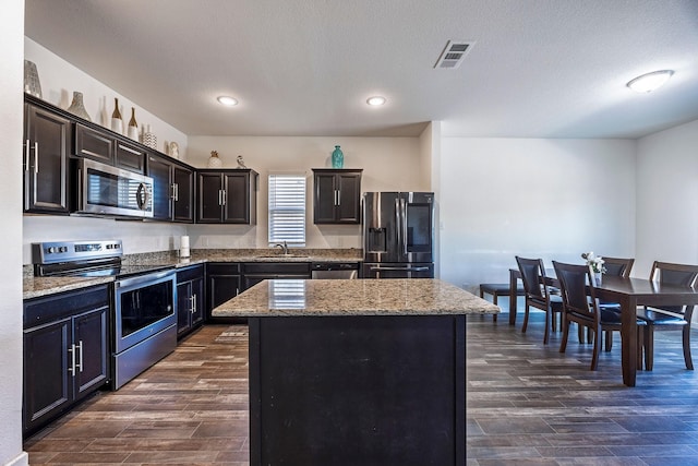 kitchen with appliances with stainless steel finishes, a center island, dark wood-type flooring, and sink