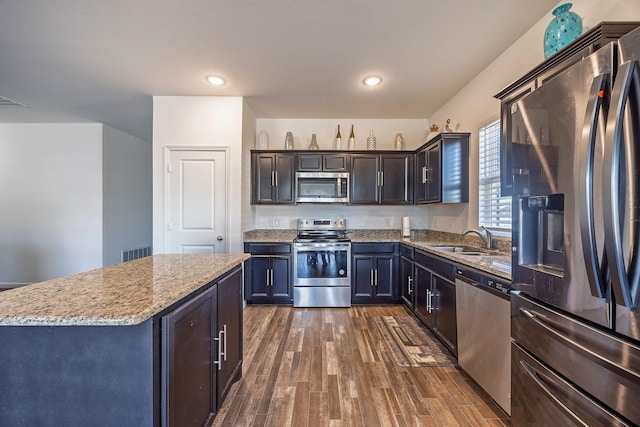 kitchen with sink, a center island, appliances with stainless steel finishes, dark hardwood / wood-style flooring, and light stone countertops