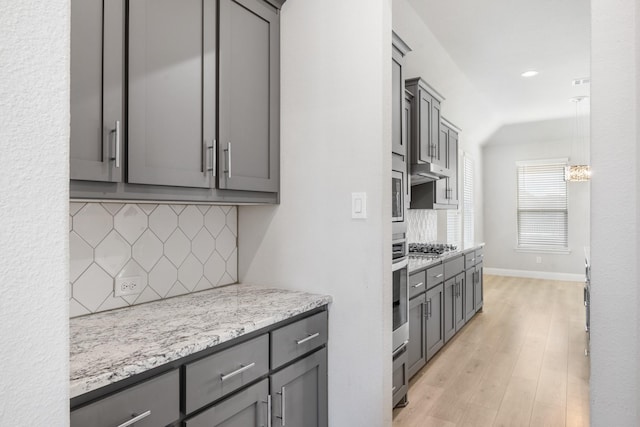 kitchen featuring light stone countertops, appliances with stainless steel finishes, backsplash, gray cabinetry, and light hardwood / wood-style floors