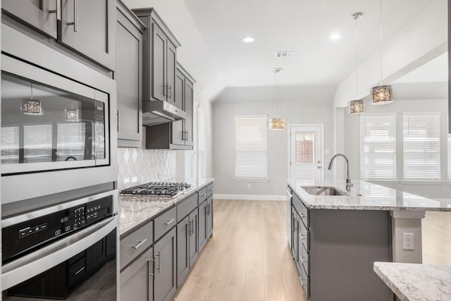 kitchen featuring sink, stainless steel appliances, tasteful backsplash, decorative light fixtures, and a kitchen island with sink