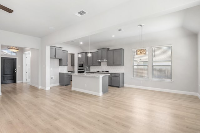 kitchen with decorative light fixtures, backsplash, a center island with sink, and gray cabinetry