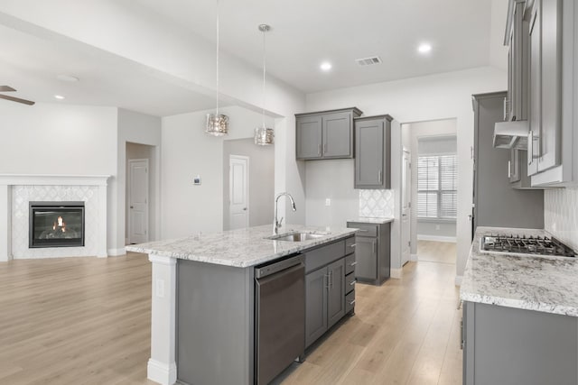 kitchen with stainless steel appliances, a kitchen island with sink, sink, pendant lighting, and a tiled fireplace