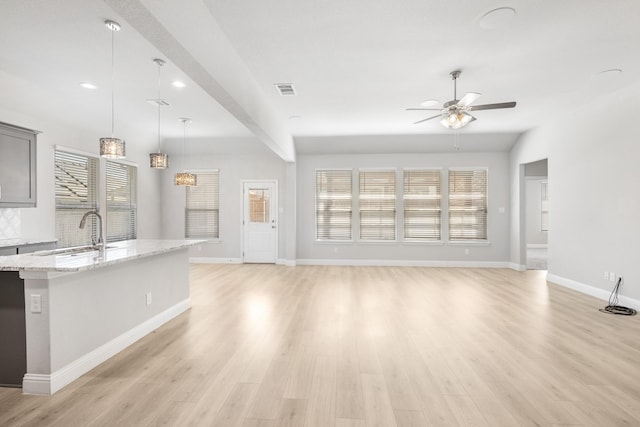 kitchen with pendant lighting, sink, ceiling fan, light stone countertops, and light wood-type flooring