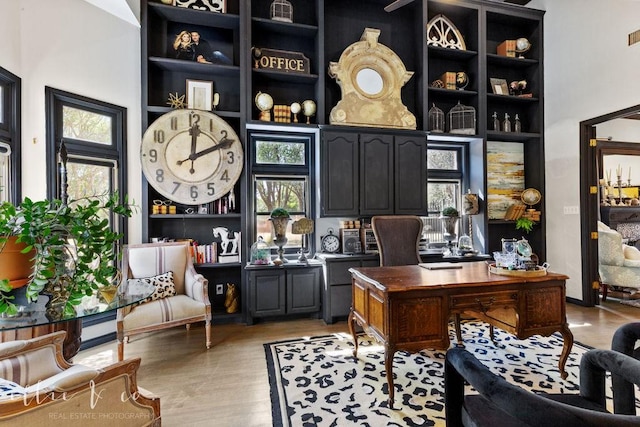 office featuring a towering ceiling, light wood-type flooring, and a healthy amount of sunlight