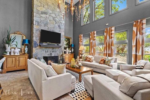 living room with a chandelier, a towering ceiling, a stone fireplace, and plenty of natural light