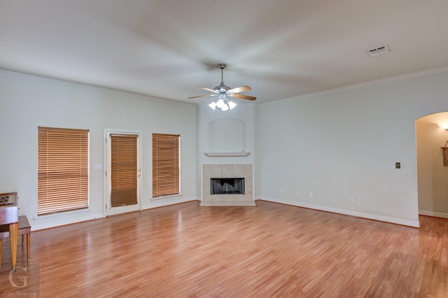 unfurnished living room with a tiled fireplace, crown molding, ceiling fan, and light hardwood / wood-style floors