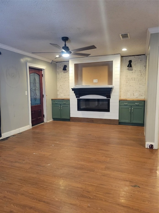 unfurnished living room with ceiling fan, a large fireplace, light hardwood / wood-style flooring, crown molding, and a textured ceiling