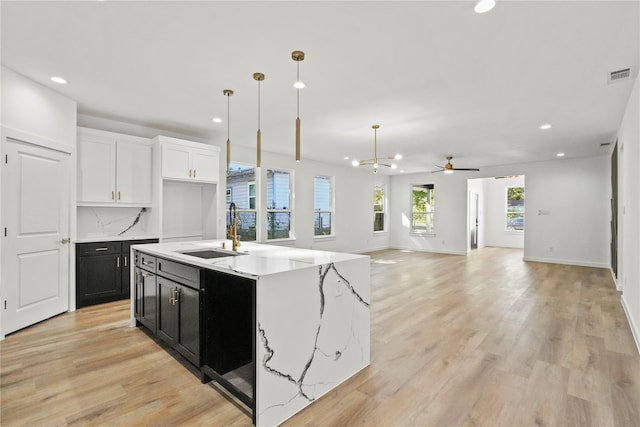 kitchen with sink, a center island with sink, light wood-type flooring, pendant lighting, and white cabinets