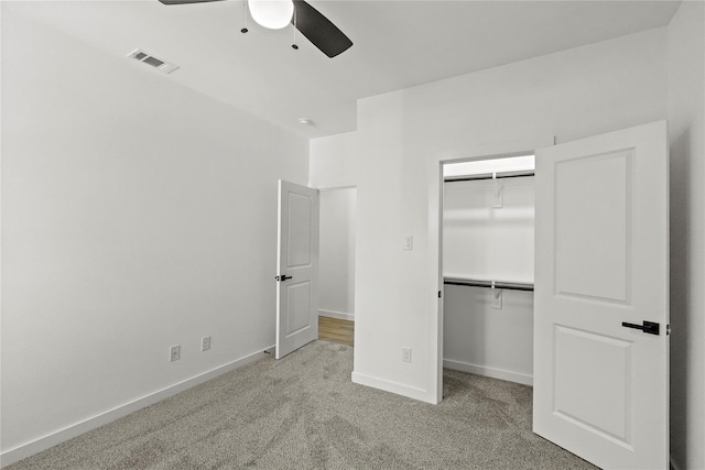 unfurnished bedroom with light carpet, a walk in closet, a closet, and ceiling fan