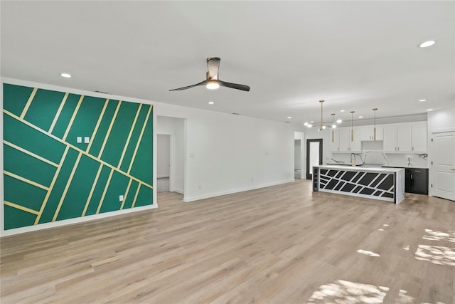 unfurnished living room featuring ceiling fan, sink, and light wood-type flooring