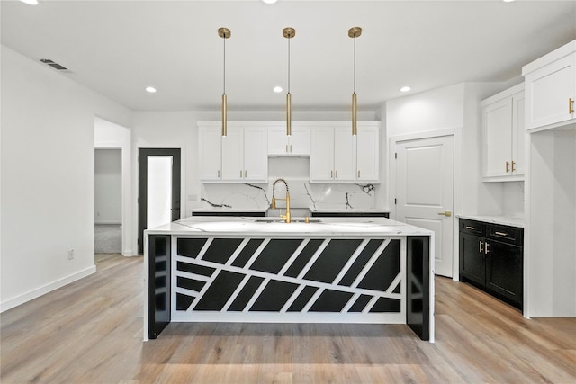 kitchen with hanging light fixtures, tasteful backsplash, a kitchen island with sink, and white cabinets