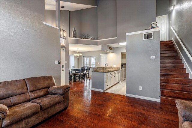 living room with a towering ceiling, a chandelier, sink, and light wood-type flooring