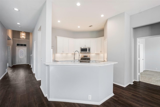 kitchen with white cabinets, dark hardwood / wood-style flooring, kitchen peninsula, and stainless steel appliances