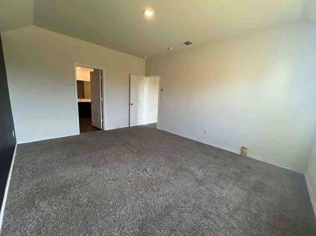 unfurnished bedroom featuring dark colored carpet, ensuite bathroom, and vaulted ceiling