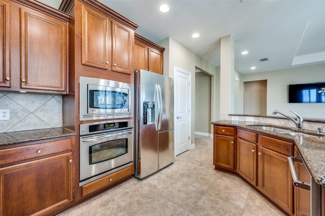 kitchen with backsplash, stone countertops, sink, and stainless steel appliances