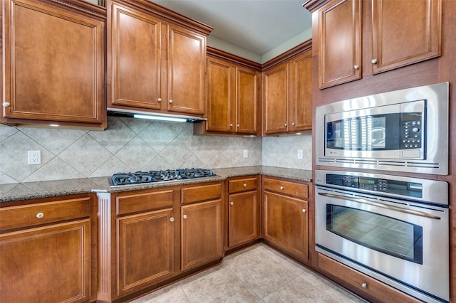 kitchen featuring backsplash, light tile patterned floors, dark stone counters, and appliances with stainless steel finishes