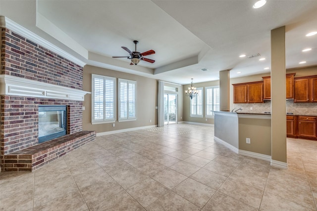 unfurnished living room with a raised ceiling, a fireplace, light tile patterned floors, and ceiling fan with notable chandelier