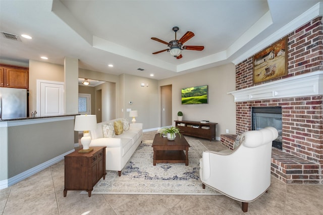 tiled living room featuring a tray ceiling, ceiling fan, and a fireplace