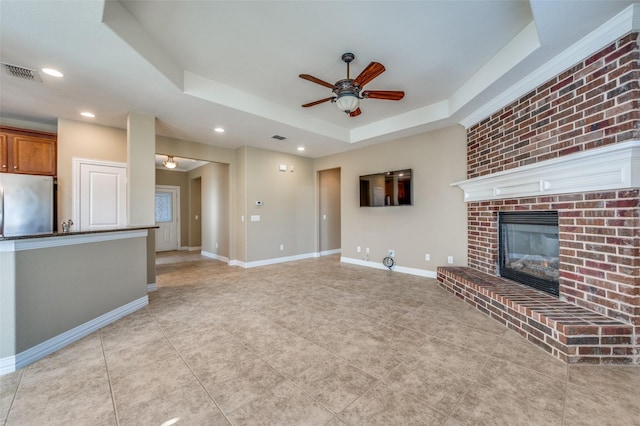 unfurnished living room featuring a fireplace, light tile patterned floors, a raised ceiling, and ceiling fan