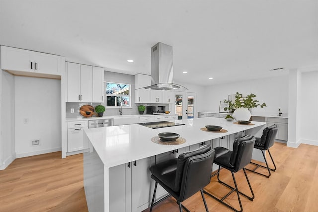 kitchen with a breakfast bar, island range hood, white cabinets, a kitchen island, and black electric cooktop