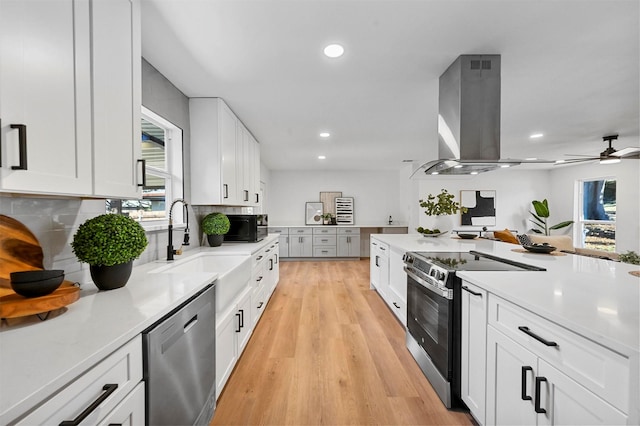 kitchen featuring island range hood, white cabinetry, backsplash, and appliances with stainless steel finishes