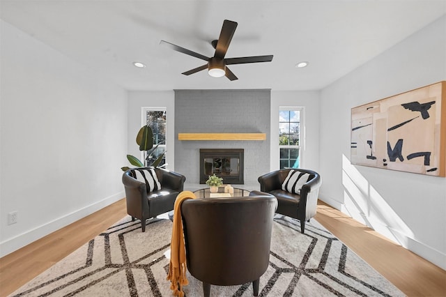 living area featuring ceiling fan, light wood-type flooring, and a fireplace