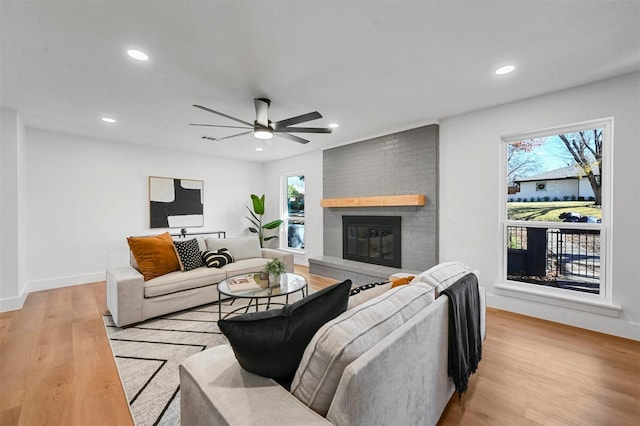 living room featuring ceiling fan, light hardwood / wood-style flooring, and a brick fireplace