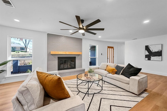 living room with ceiling fan, a fireplace, and light hardwood / wood-style flooring