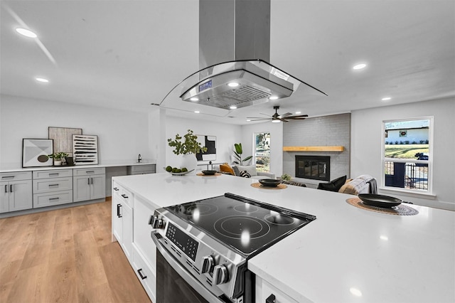 kitchen with island exhaust hood, white cabinets, light hardwood / wood-style flooring, a fireplace, and stainless steel range with electric cooktop