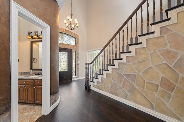 foyer entrance with wood-type flooring, a towering ceiling, sink, and an inviting chandelier