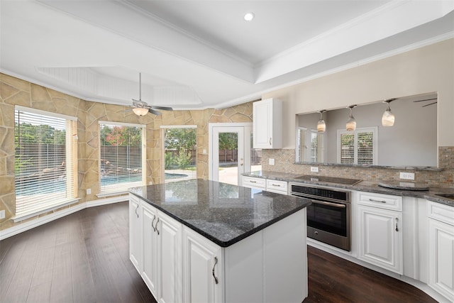 kitchen with white cabinetry, stainless steel oven, dark stone counters, and a tray ceiling