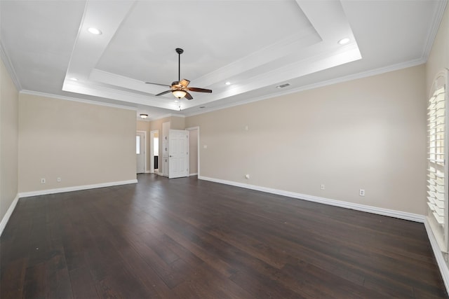 empty room with dark hardwood / wood-style floors, ceiling fan, a tray ceiling, and crown molding