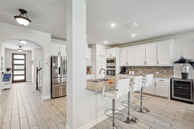 kitchen featuring wine cooler, sink, stainless steel appliances, light stone countertops, and white cabinets