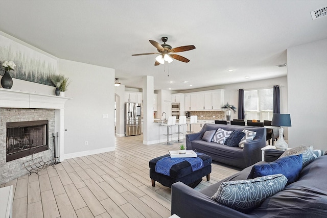 living room featuring a stone fireplace, ceiling fan, and light hardwood / wood-style flooring