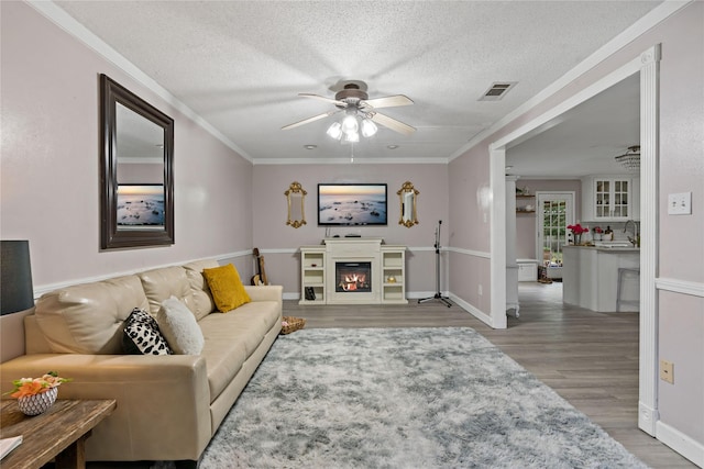 living room with wood-type flooring, a textured ceiling, ceiling fan, and ornamental molding