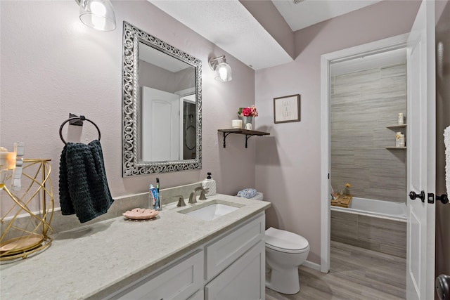 bathroom with tiled tub, vanity, wood-type flooring, and toilet