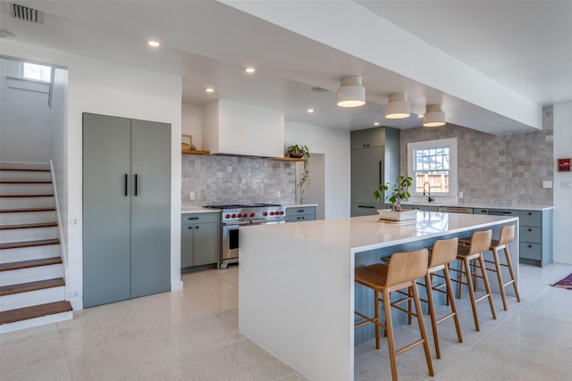 kitchen featuring gray cabinetry, a kitchen island, tasteful backsplash, a breakfast bar, and stainless steel stove