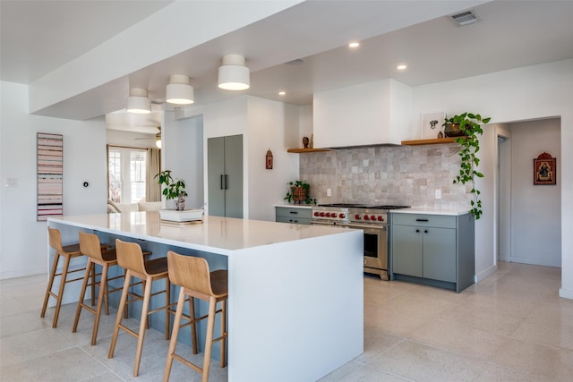 kitchen featuring decorative backsplash, a breakfast bar, ceiling fan, high end stainless steel range, and gray cabinets