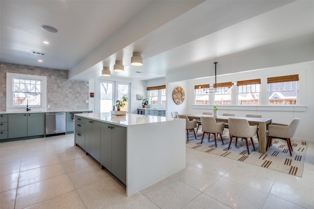 kitchen with hanging light fixtures, stainless steel dishwasher, gray cabinets, plenty of natural light, and a kitchen island