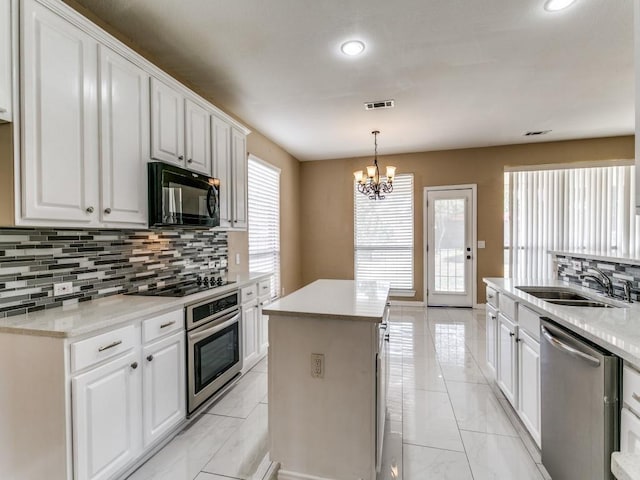 kitchen with sink, a kitchen island, a notable chandelier, white cabinets, and black appliances