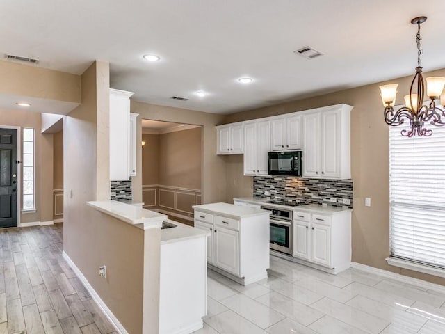 kitchen with pendant lighting, black appliances, white cabinets, tasteful backsplash, and kitchen peninsula